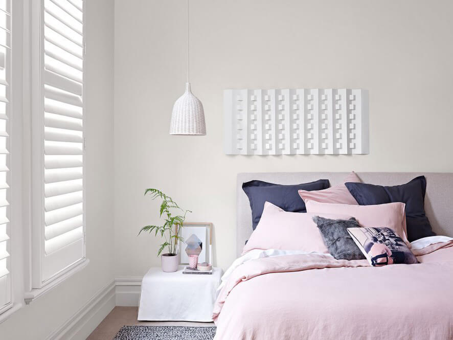 White walls bedroom with pink bedding and pillows with beside table and hanging light and plant